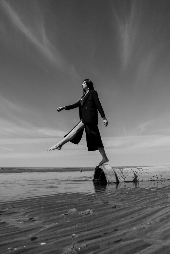 Black and white image of a female stepping off drift wood on a beach in self transformation.