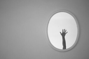 Black and white image with a raised hand in a mirror. Photo by emre-can-acer on pexels.