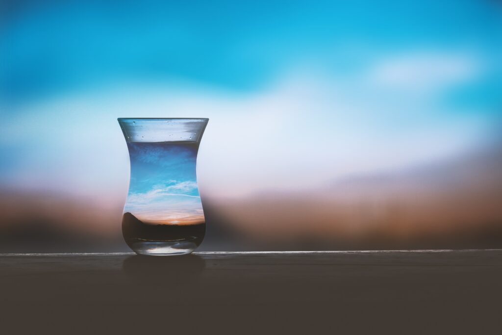 A glass reflecting the sky that is obscured in the background to symbolize a glass half full in attracting better clients for business.  